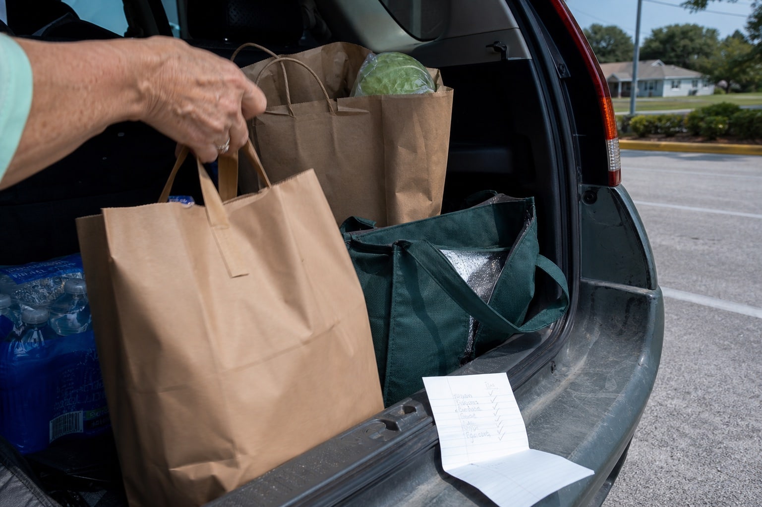 Grocery bags and a checked list in an open car trunk.